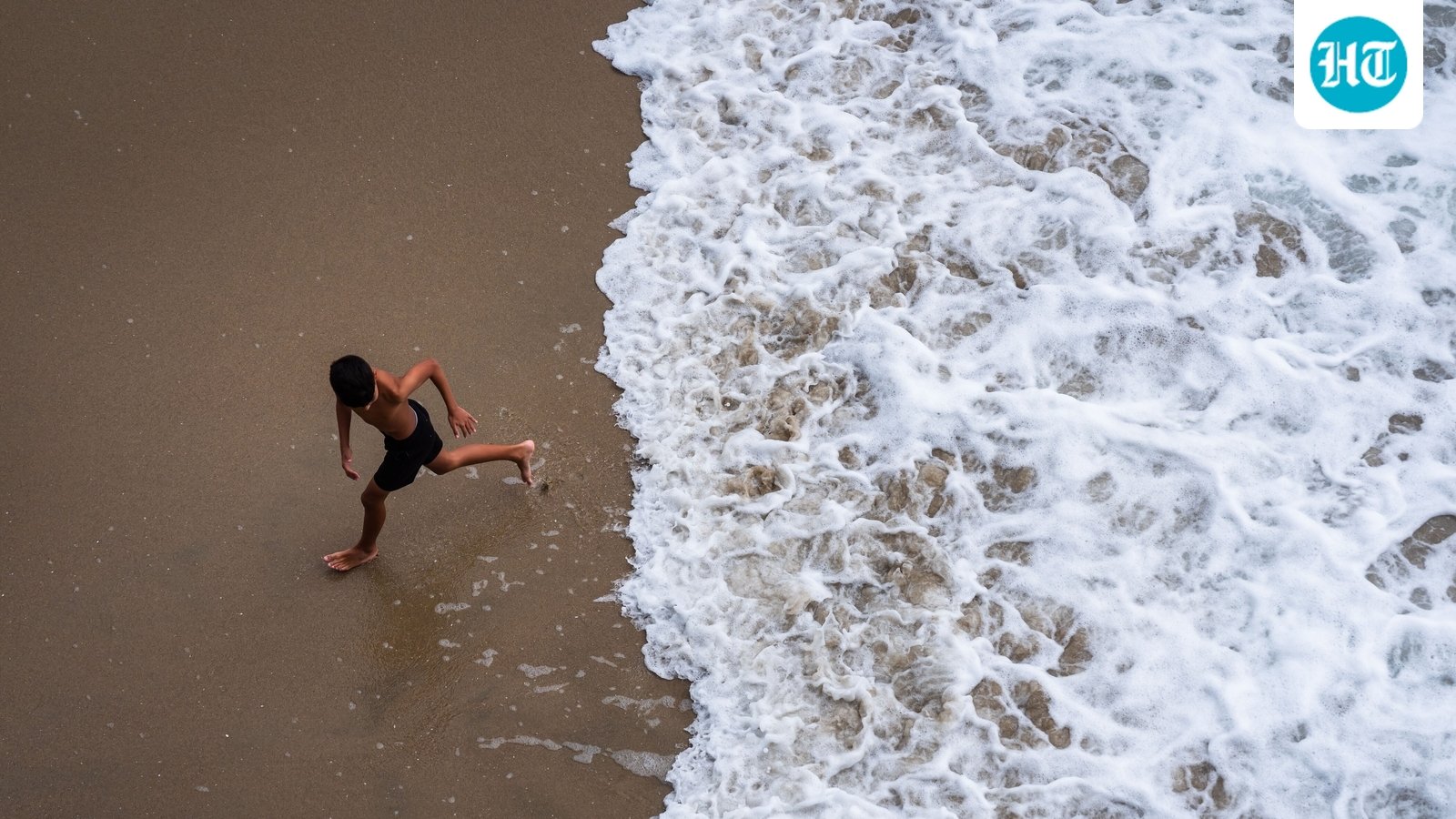 A child runs from the water as large waves break on the shore on Huntington Beach, southern California. (AP Photo/Ethan Swope)